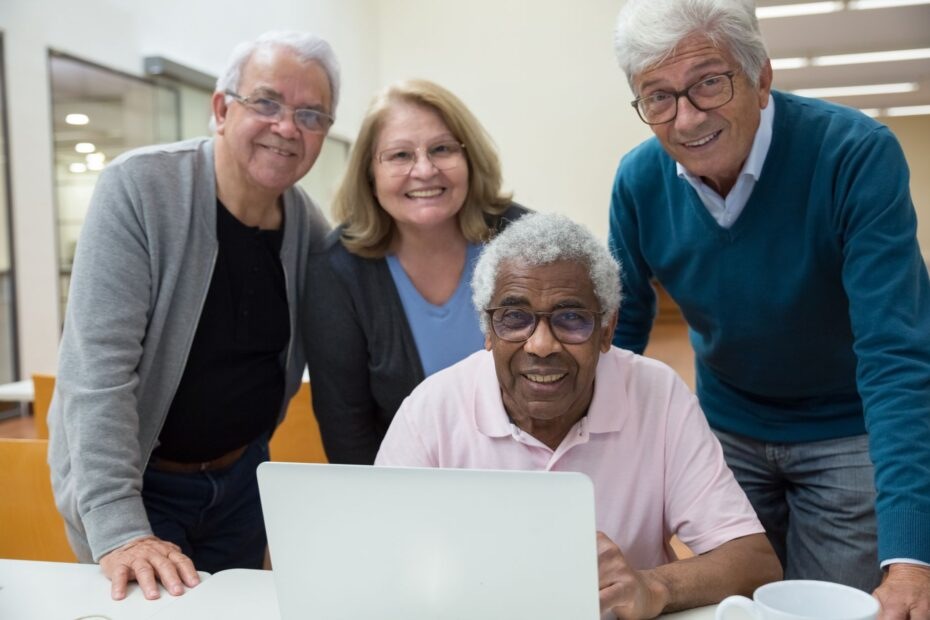 group of elderly people standing behind a laptop and smiling