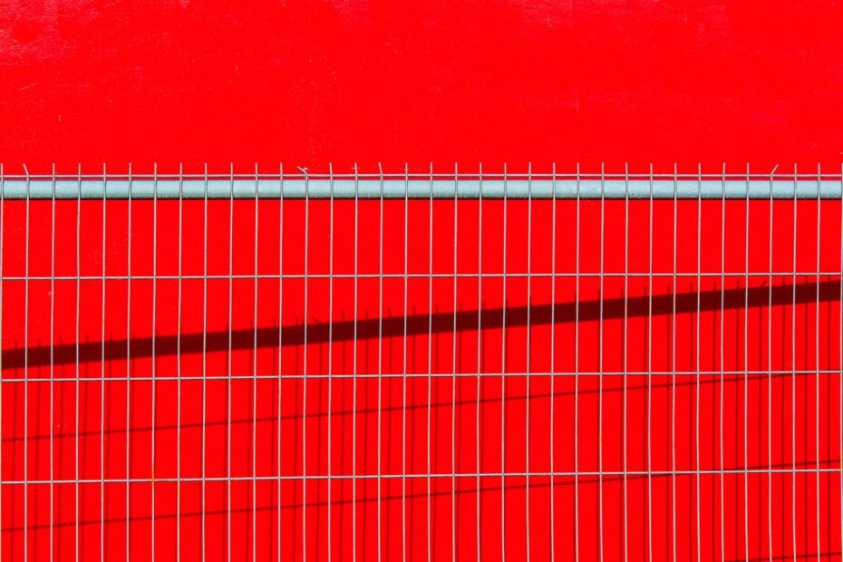 close up of a metal fence on the background of a bright red wall
